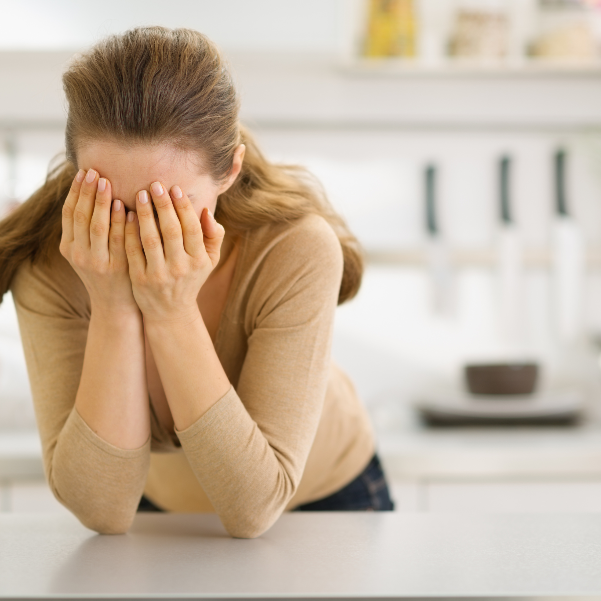 frustrated or defeated mom with face in hands at kitchen counter