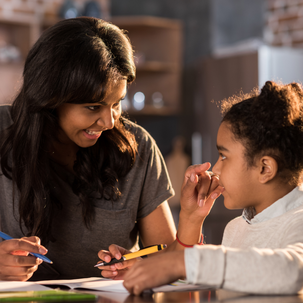 mom and daugther with school work in front of them, looking at each other and smiling