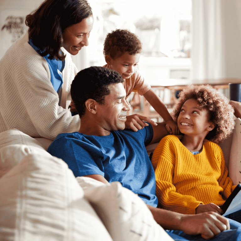 happy family on couch with kids making eye contact with parents, looking up at them. Family members are smiling.