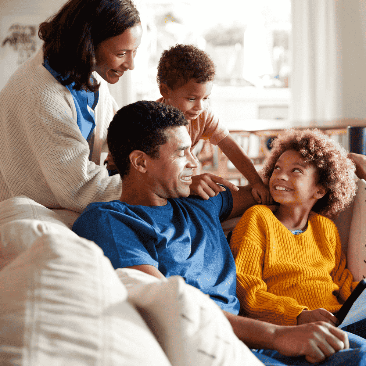 happy family on couch with kids making eye contact with parents, looking up at them. Family members are smiling.