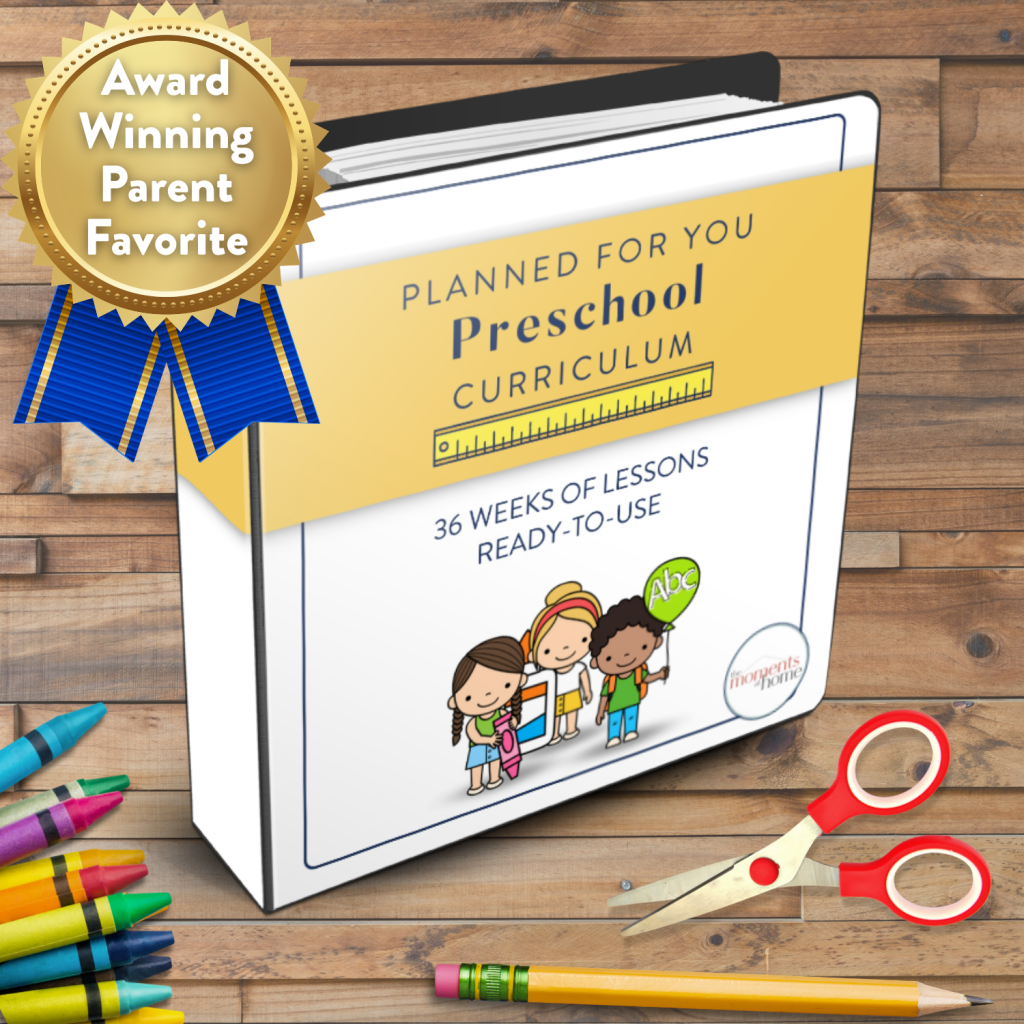 mockup of The moments At Home Preschool in a binder on a wooden background with school supplies, as well as a blue ribbon in the top left that says "Award Winning Parent Favorite"